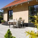Deck with table and chairs in front of a brick house with red roof.