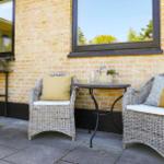 Terrace with two wicker chairs, table, and plants against a yellow brick house.