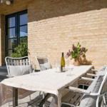Terrace with table, chairs, flowers, and wine bottle against brick wall.