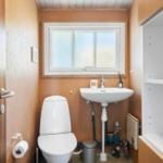 Badezimmer mit Toilette, Waschbecken und Fenster. Holzwände und weißer Einbau.