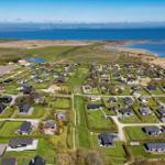 Luftbild eines Ferienortes mit Häusern, Grünflächen und Blick auf Meer und Windkraftanlagen.