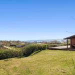Haus mit Terrasse, Grünfläche und Blick auf Wasser und Dorf.