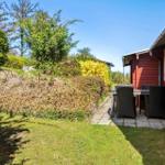 Roter Holzaufbau mit Terrasse, Tisch und Stühlen. Grasfläche und Hecken im Hintergrund.