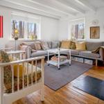 Living room with sofa, chairs, and windows. Wooden floor and wall art.
