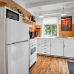 Kitchen with white countertop, refrigerator, stove, and window with view of greenery.