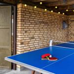 Ping pong table with paddles and ball in a room with brick wall and string lights.