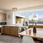 Kitchen with wooden cabinets and dining table. Windows overlook the outdoor area.
