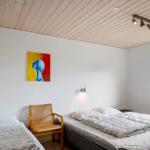 Room with two beds, wooden ceiling, wall art, and window with view of green.