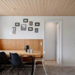 Dining area with wooden table, black chairs, and wall pictures. Wooden ceiling and window view.