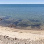 Beach with gravel and sand, clear water, horizon in the distance.