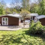 Wooden house with terrace and garden. Outdoor tables with chairs. Surrounded by trees.