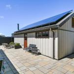 House with solar panels, terrace, and garden furniture under blue sky.