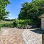 Paved path leads to a wooden cabin with garden and forest view.