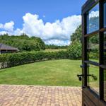 From the door, you see a green lawn with hedge and trees under blue sky.
