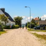 A family walks along a gravel path past houses and greenery.