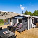 Terrace with umbrella, loungers, and table. House with gray siding and white window frames.
