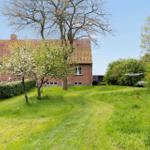 Red brick house with garden and trees under blue sky.