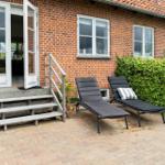 Red brick house with terrace, two lounge chairs, and green hedge.