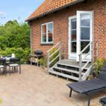 Terrace with table, chairs, lounge chairs, and grill in front of a brick house.