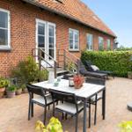 Backyard with table, chairs, sun loungers, and grill. Red brick building with white windows.