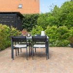 Terrace with table and chairs, surrounded by greenery and a grill.