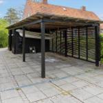 Shaded carport with boat, paved yard, and green surroundings.
