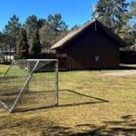 Holzhütte mit Dach aus Stroh, Fußballtor im Vordergrund, umgeben von Bäumen und Gras.