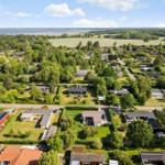Aerial view of a residential area with houses, green spaces, and water in the distance