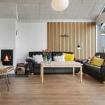 Living room with two sofas, wooden floor, and fireplace. Wood wall and large windows.