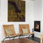 Two wicker chairs with cushions stand before a fireplace with burning fire.