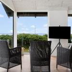 Three black wicker chairs and a TV on a stand in a room with a view of the landscape.