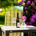 Ein Tisch mit Weinflasche, Gläsern und Blumen im Garten.
