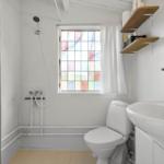 Bathroom with toilet, sink, and shower. Window with colored glass panes.