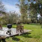 Deck with grill, table and chairs in garden. Lawn and trees in background.