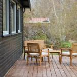 Deck with wooden bench and two chairs in front of a house with dark wood cladding.