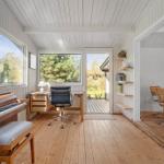 Room with piano, desk, and view of garden. Wooden floor and white walls.