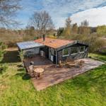 Wooden house with terrace, garden, and barbecue area in greenery.