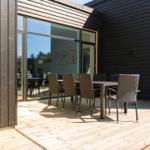 Terrasse mit Tisch und Stühlen vor modernem Haus mit Glasfront.