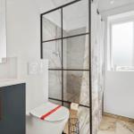 Badezimmer mit Dusche, Toilette und Waschbecken. Fenster und Marmorfliesen.