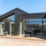Moderne Holzhütte mit großem Terrassenbereich und Sitzgelegenheiten.