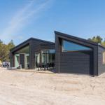 Moderne schwarze Hütte mit großem Glasbereich und Außenterrasse im Wald.