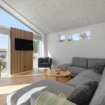 Ein Wohnzimmer mit grauem Sofa, runder Tisch und großen Fenstern.
