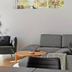 Ein Wohnzimmer mit grauem Sofa, Holztisch und Sessel. An der Wand hängt ein Bild mit Blumen.