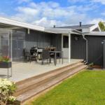 Deck with grill, table and chairs. Black wood wall and green lawn.