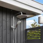 Outdoor shower with shower head and handheld shower at gray wooden house.