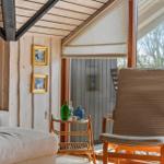 Ein Raum mit Holzwand und -decke, einem Sessel und einem Sofa. Durch das Fenster ist eine Terrasse sichtbar.