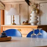 Runder Tisch mit blauen Stühlen, Kerzen und Gläsern vor Holzwand und Schrank.