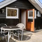 Haus mit Terrasse, Tisch und Stühlen. Tür offen. Holzwand und Dach.