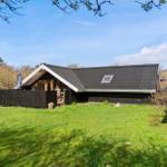 Ein Haus mit dunklem Dach und Holzverkleidung, umgeben von Gras und Bäumen.