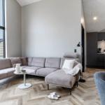 Wohnbereich mit grauem Sofa, Holzboden und Blick auf Baustelle.